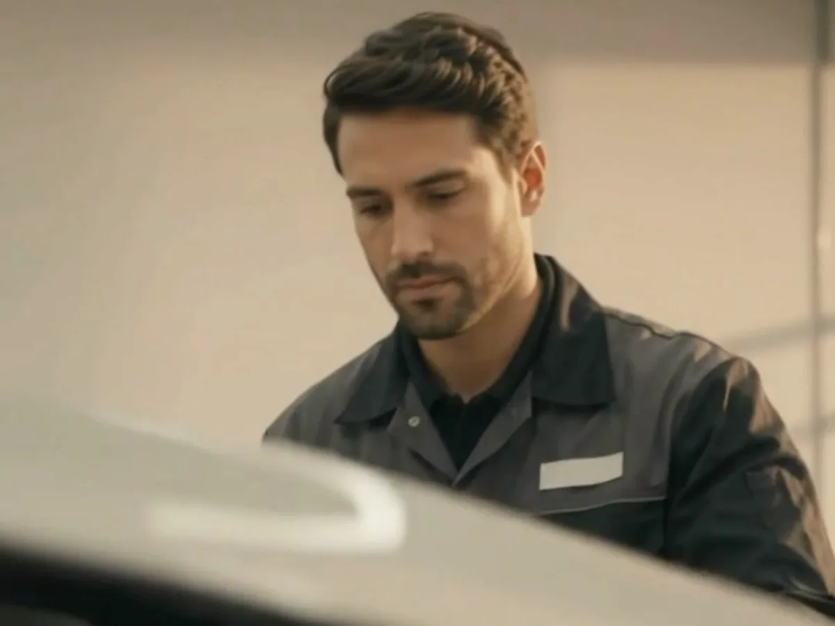 Mechanic inspecting a car under a raised hood, from a CAR by Aquarius video